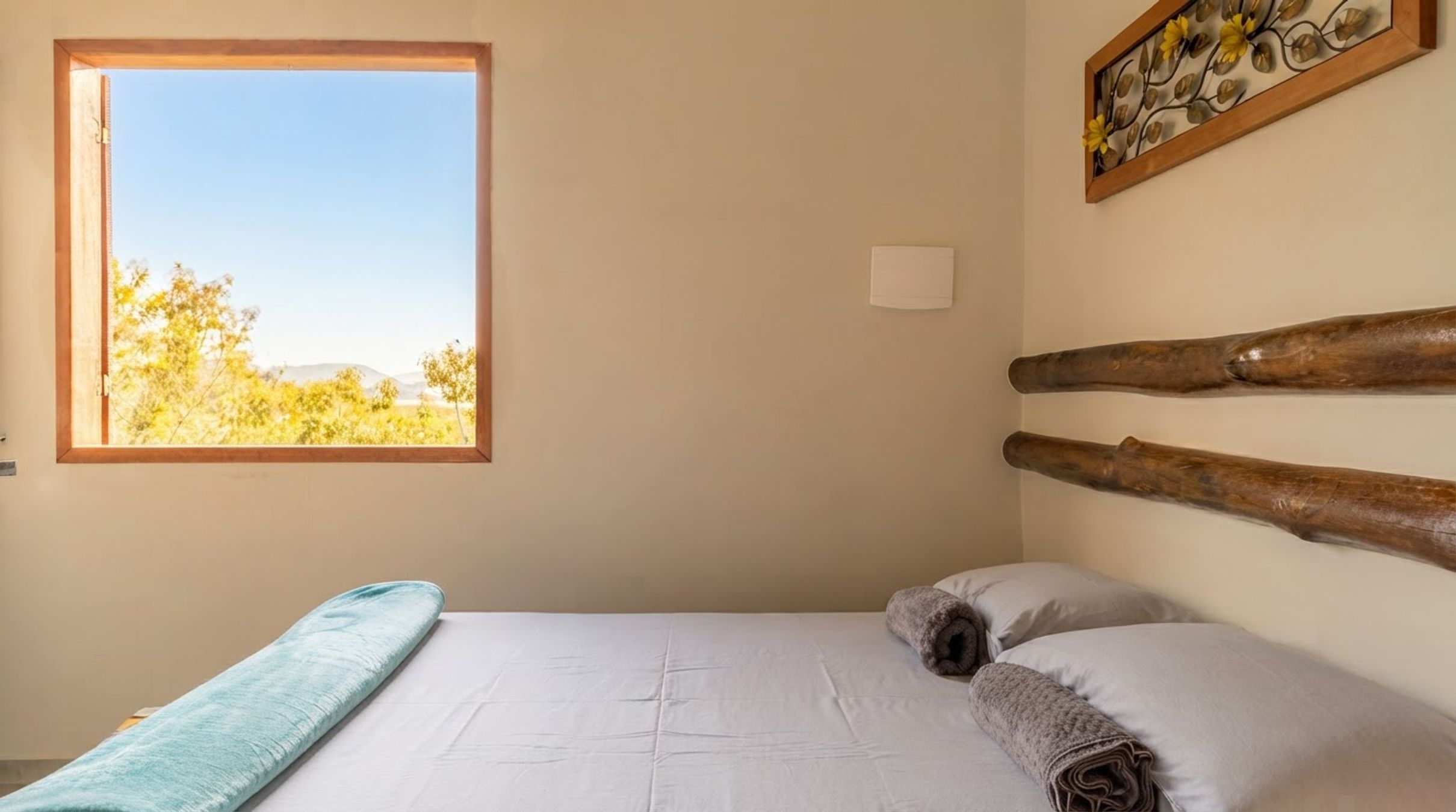 A bedroom with a single bed, a window with a view of trees, and a wall-mounted artwork.