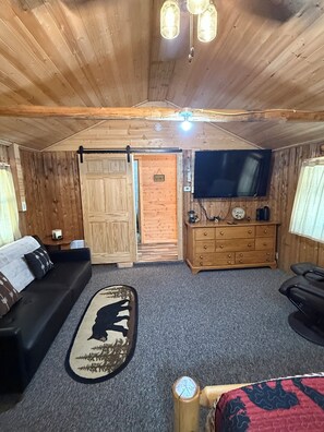 Ein gemütliches Zimmer mit Holzbalkendecke, einem Flachbildfernseher, einer Holzkombination, einem Sofa und einem Teppich mit Bärenmotiv.