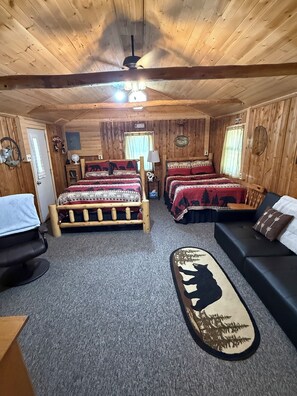 Ein rustikales Zimmer mit zwei hölzernen Betten, einer Couch, einem Schreibtisch und einem Deckenventilator.