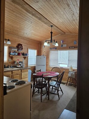 Ein Holzblockhaus-Innenraum mit Küchenbereich, der einen Herd, einen Kühlschrank und einen Esstisch mit Stühlen zeigt.