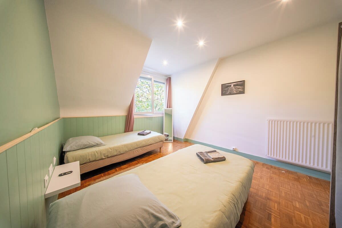 A room with two beds, a window, a radiator, and a picture on the wall.