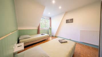 A room with two beds, a window, a radiator, and a picture on the wall.