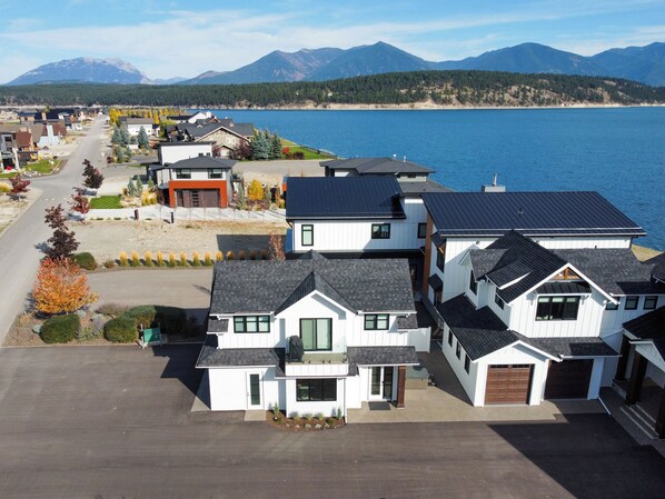 A residential area with houses, a road, and a lake with mountains in the background.
