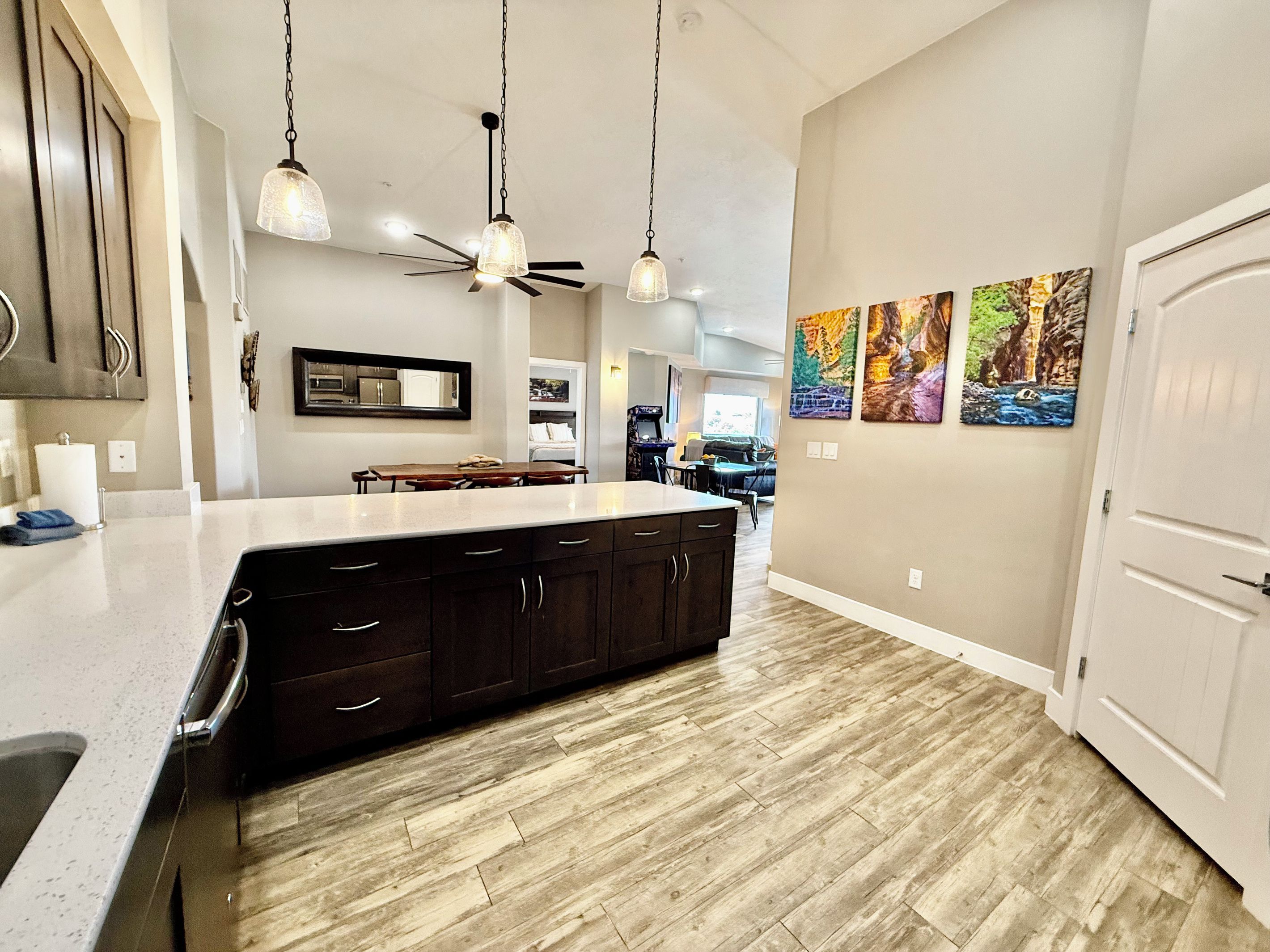 A kitchen with a large island, dark wooden cabinets, pendant lighting, and artwork on the wall.