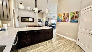 A kitchen with a large island, dark wooden cabinets, pendant lighting, and artwork on the wall.