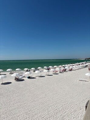 Een strand met witte parasols en ligbedden, een heldere lucht en de oceaan op de achtergrond.
