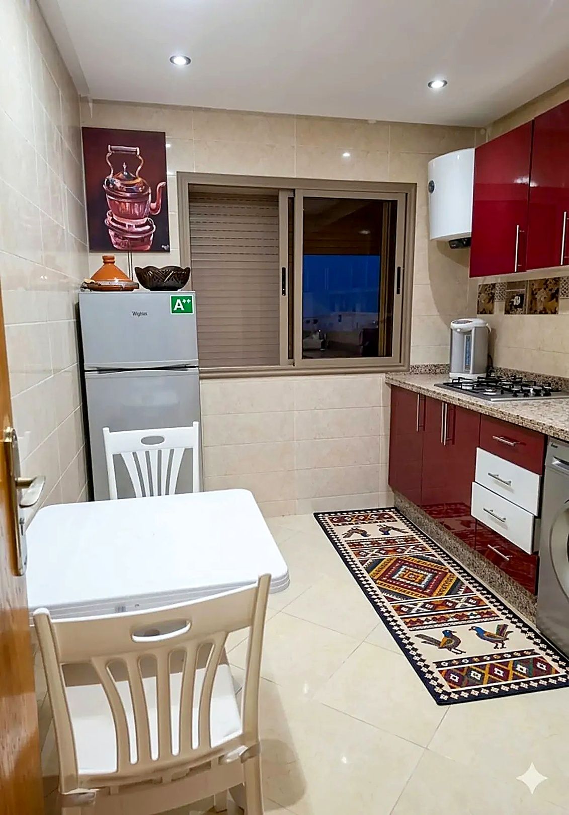A compact kitchen with a refrigerator, a window, a stove, and a dining area with a table and chairs.
