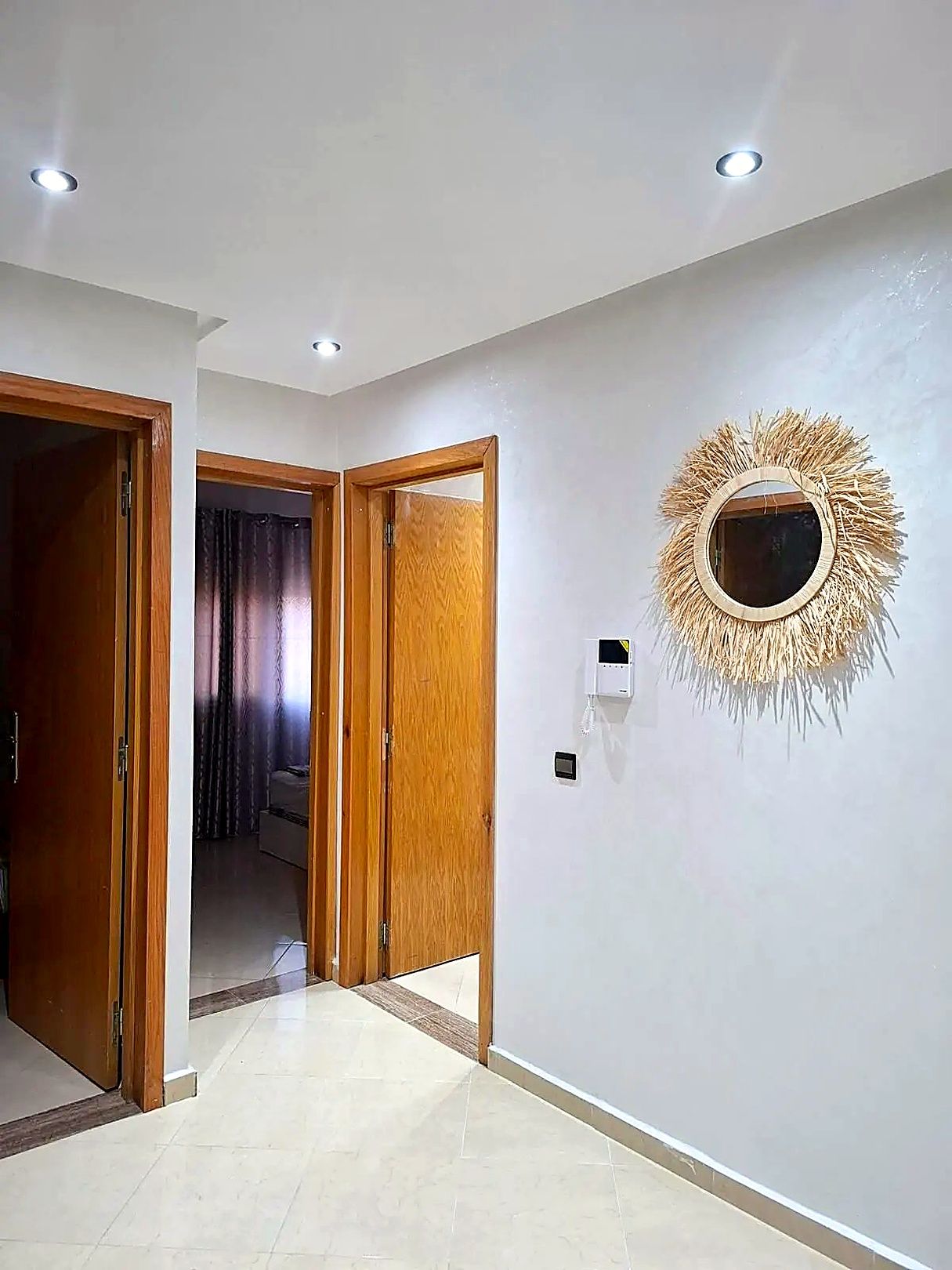 A hallway with wooden doors, a wall-mounted light fixture, and a decorative mirror.