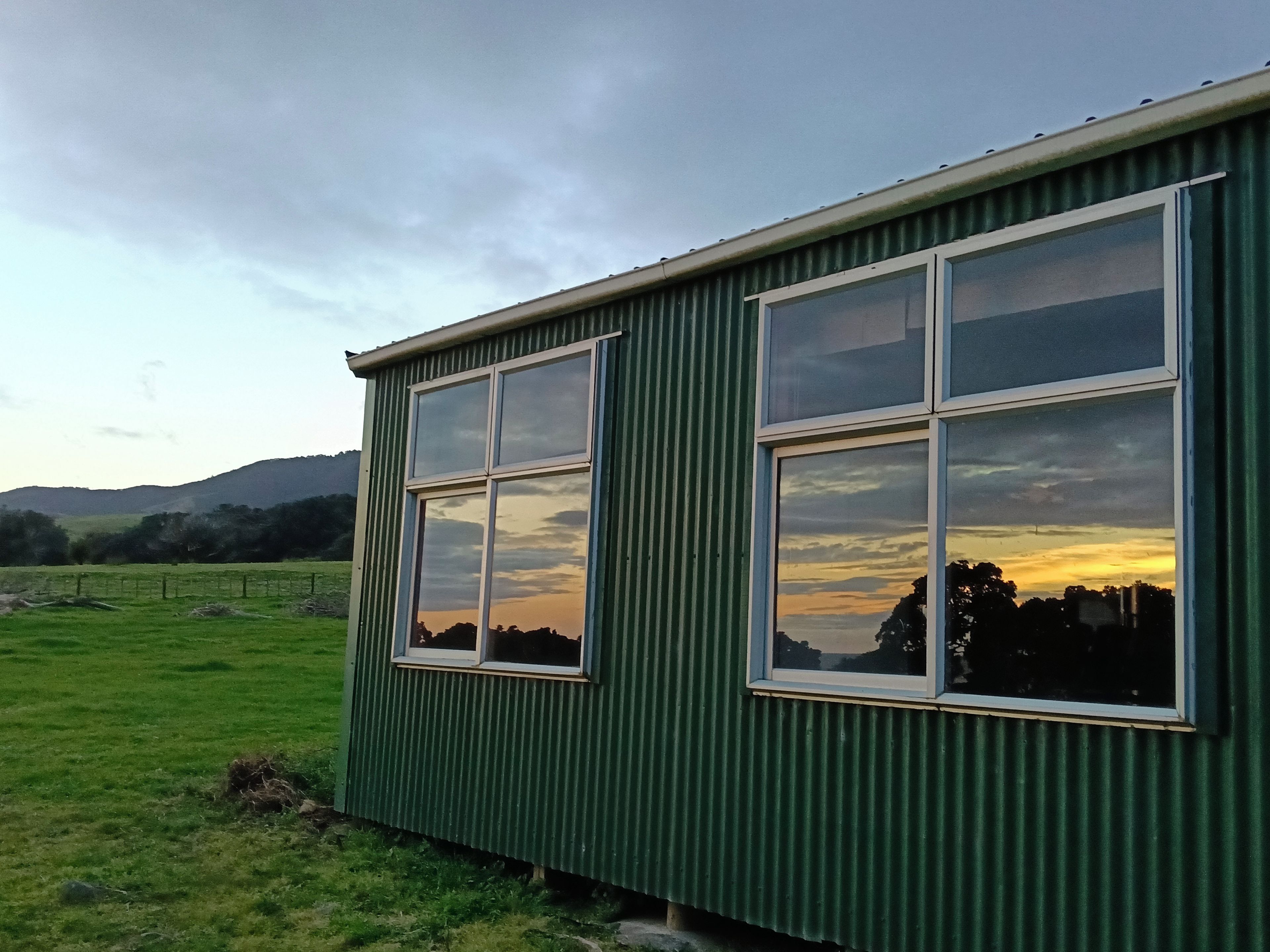A green building with large windows, a grassy field, and hills in the background.