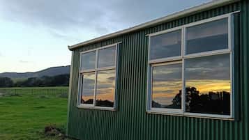 A green building with large windows, a grassy field, and hills in the background.