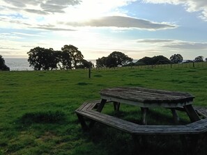 A picnic table in a grassy field with a view of the sea and trees in the background.