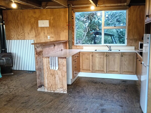 A kitchen with wooden cabinets, a countertop, a window with a view of trees, and a white appliance.
