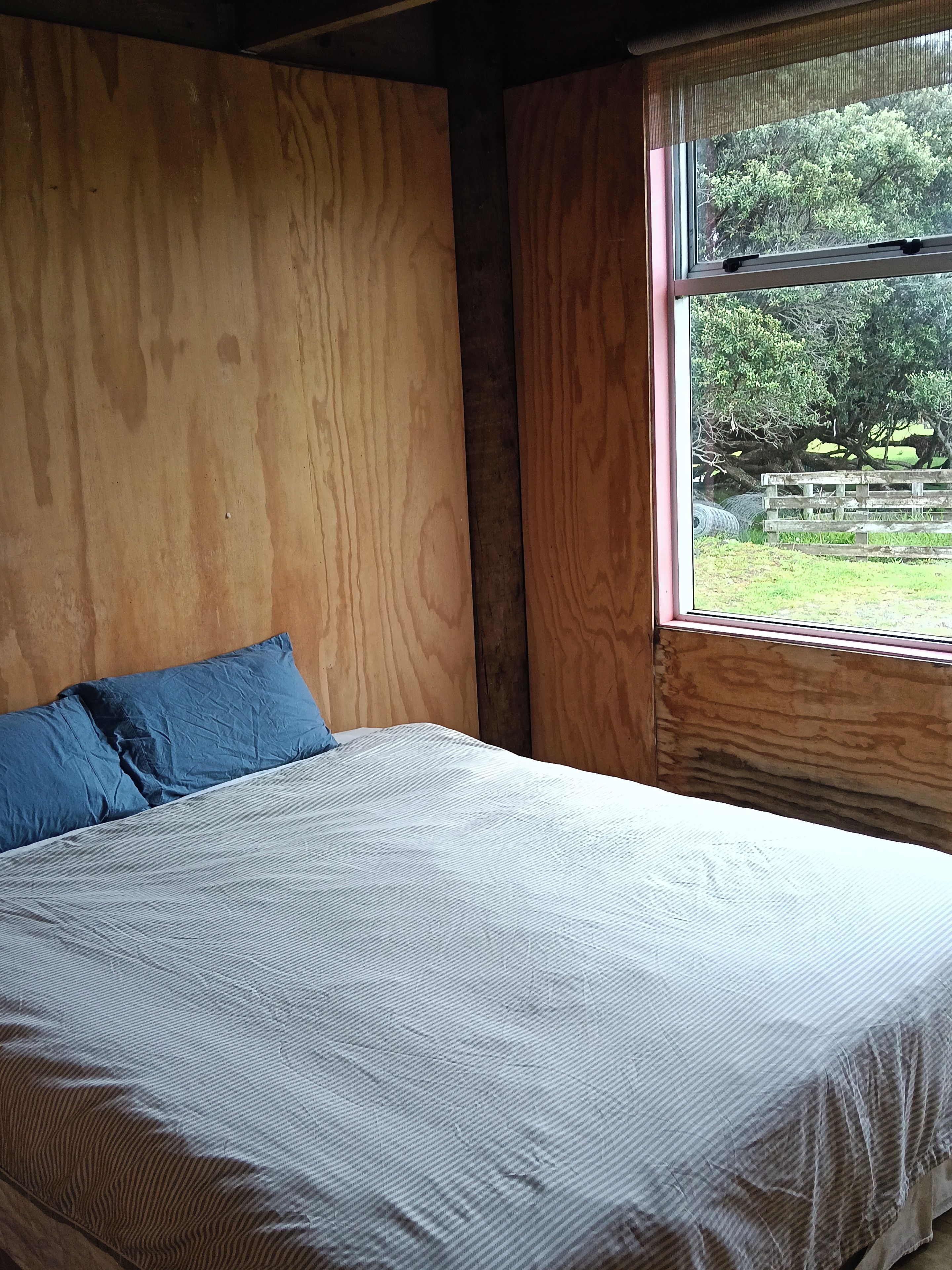 A bedroom with a wooden headboard, a bed with a striped bedspread, and a window with a view of trees and a fence.