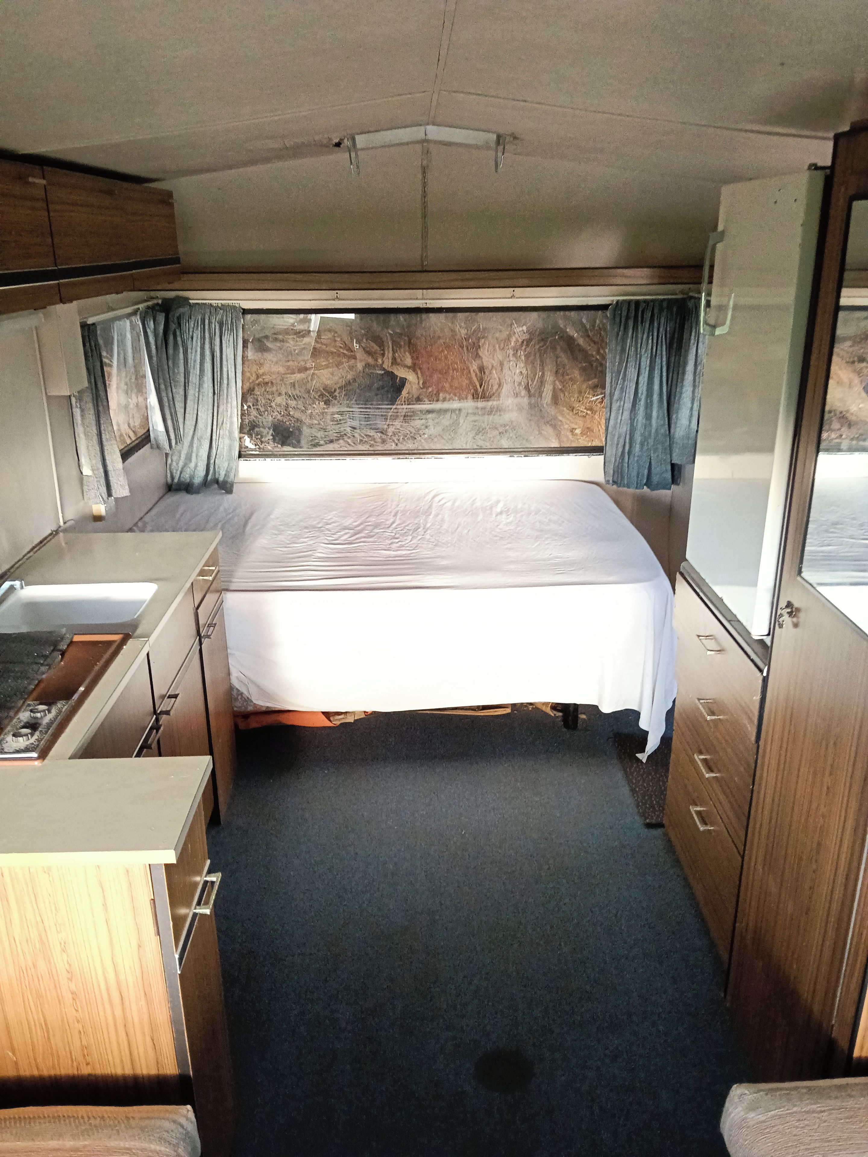 A compact bedroom with a bed, a small kitchenette, and a window with curtains.