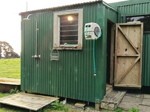 Une petite structure métallique verte, dotée d’une fenêtre, d’une porte en bois et d’un espace douche.