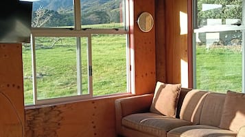A wooden interior with a sofa, a table, and large windows offering a view of a green landscape.