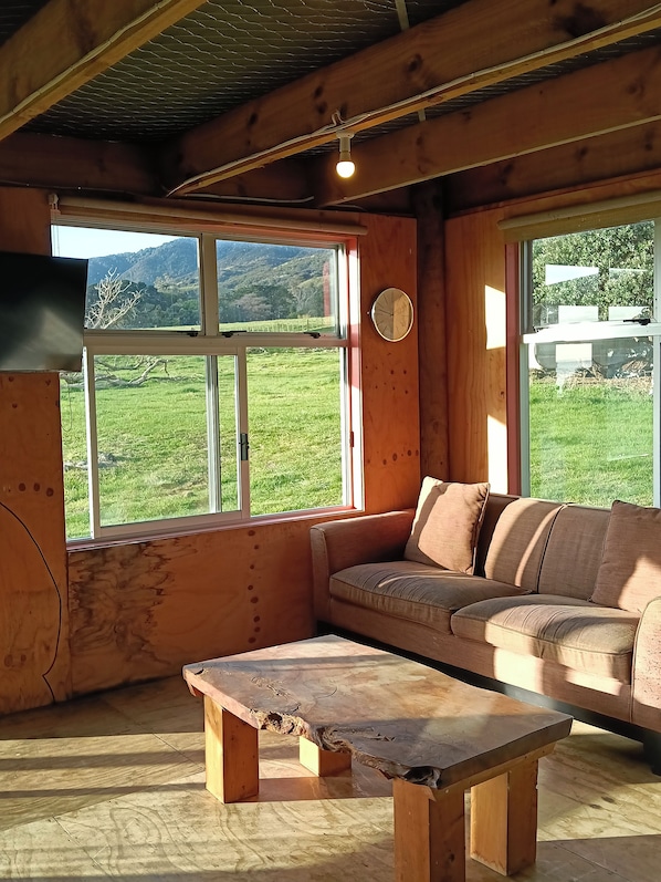 Un intérieur en bois avec un canapé, une table et de grandes fenêtres donnant sur un paysage verdoyant.