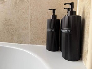 Dos botellas negras con dosificadores, etiquetadas 'SHAMPOO' y 'CONDITIONER,' sobre una bañera blanca.