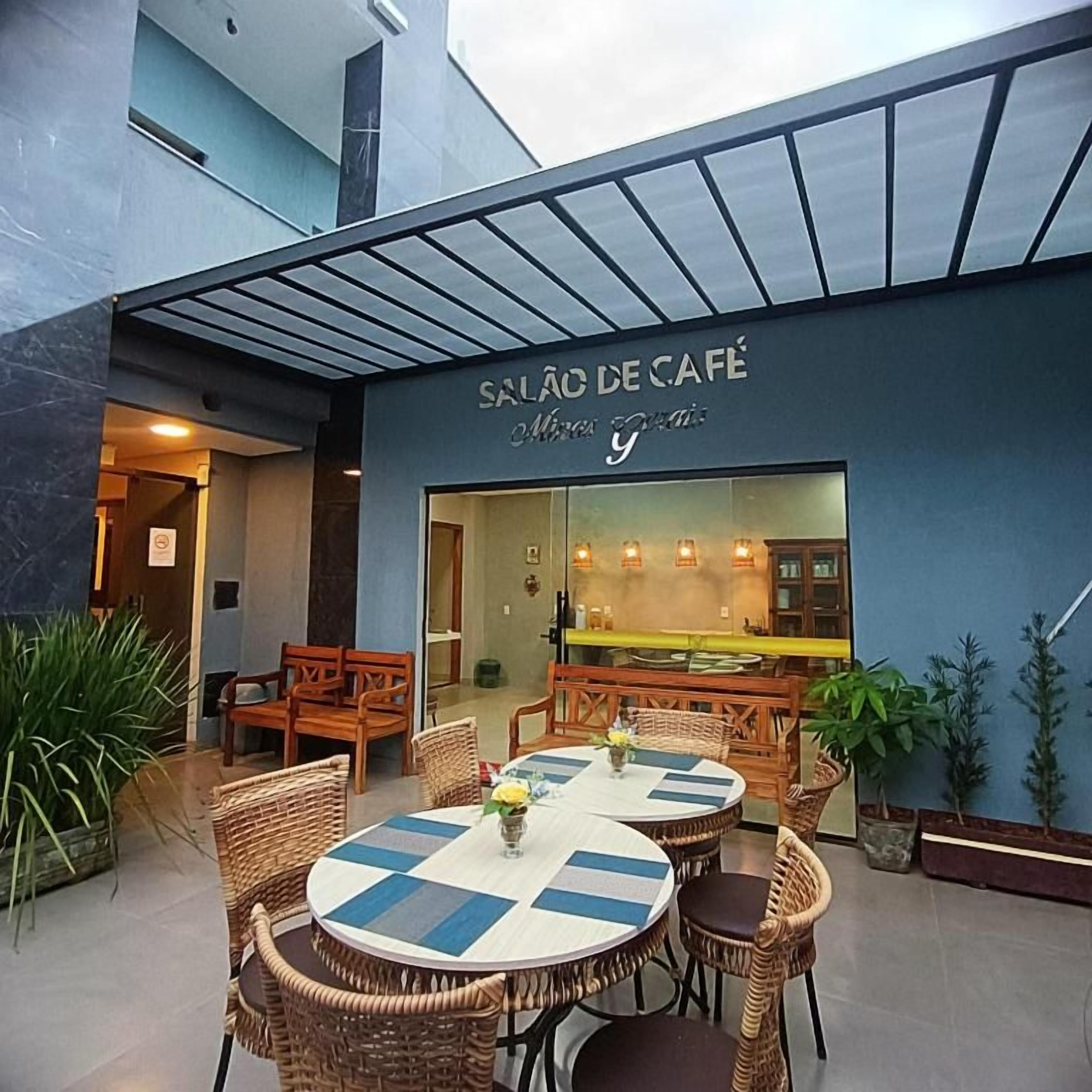 An outdoor seating area with wicker furniture and a checkered tablecloth, a café sign, and potted plants.