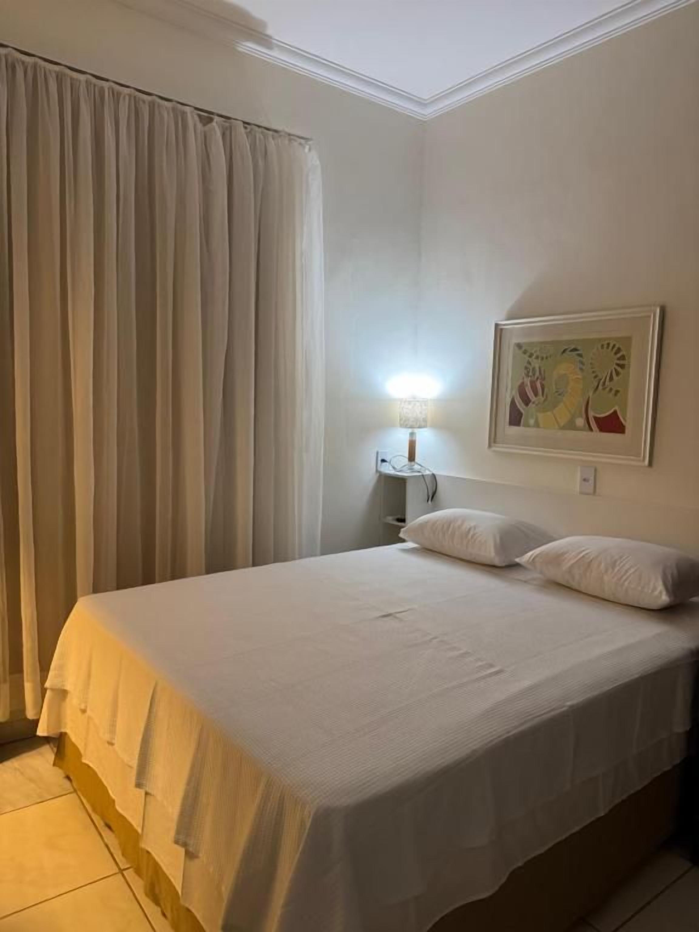 A bedroom with a bed, curtains, a lamp, and a painting on the wall.