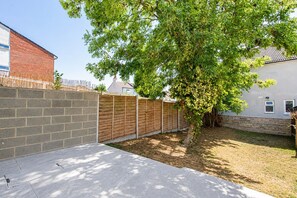 Un patio trasero con un árbol, un muro de ladrillo y una valla de madera.