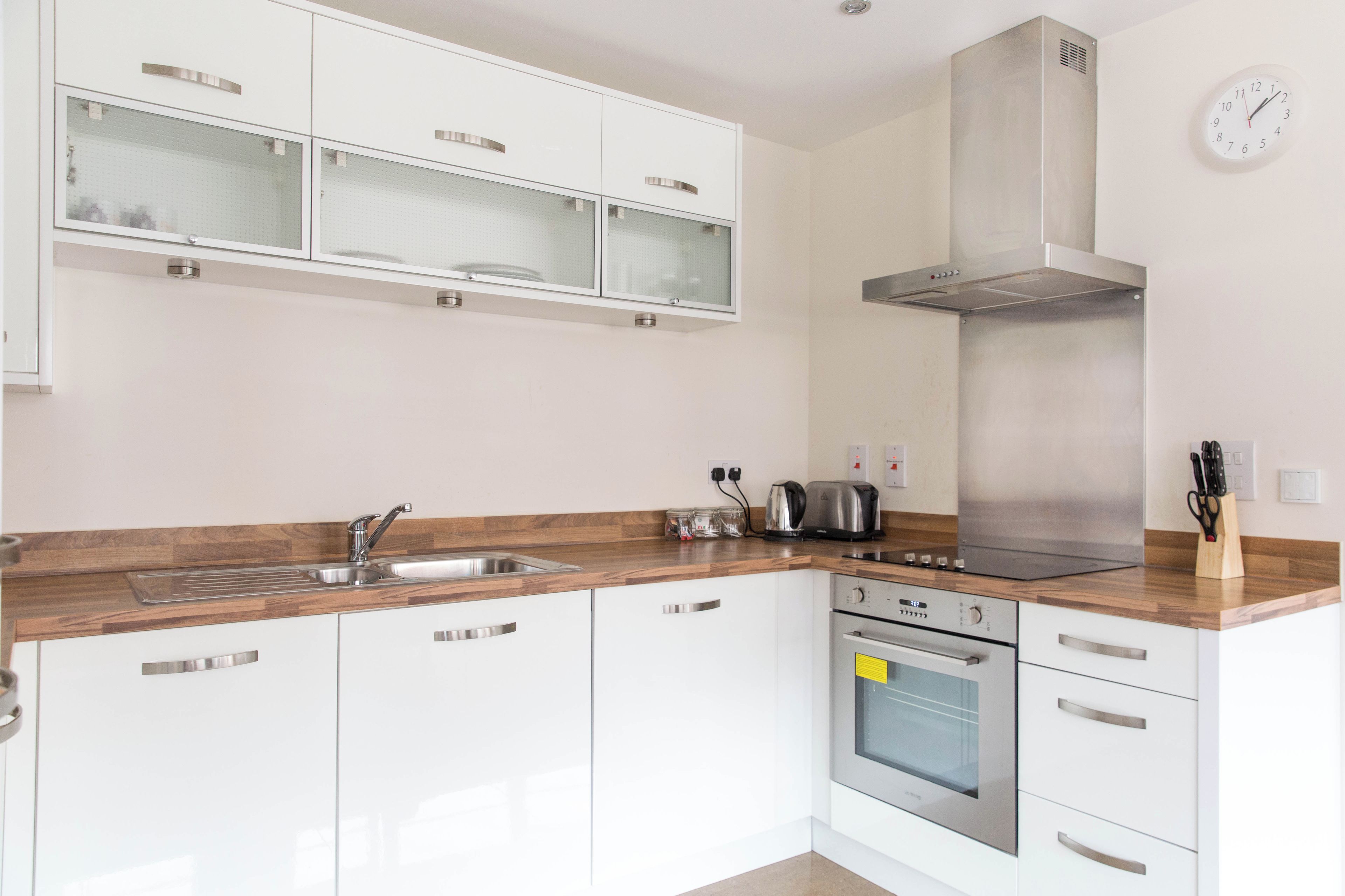 A modern kitchen with white cabinetry, a stainless steel range hood, a built-in oven, and a wooden countertop.