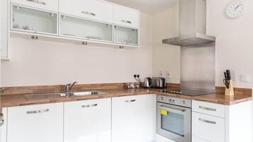 A modern kitchen with white cabinetry, a stainless steel range hood, a built-in oven, and a wooden countertop.