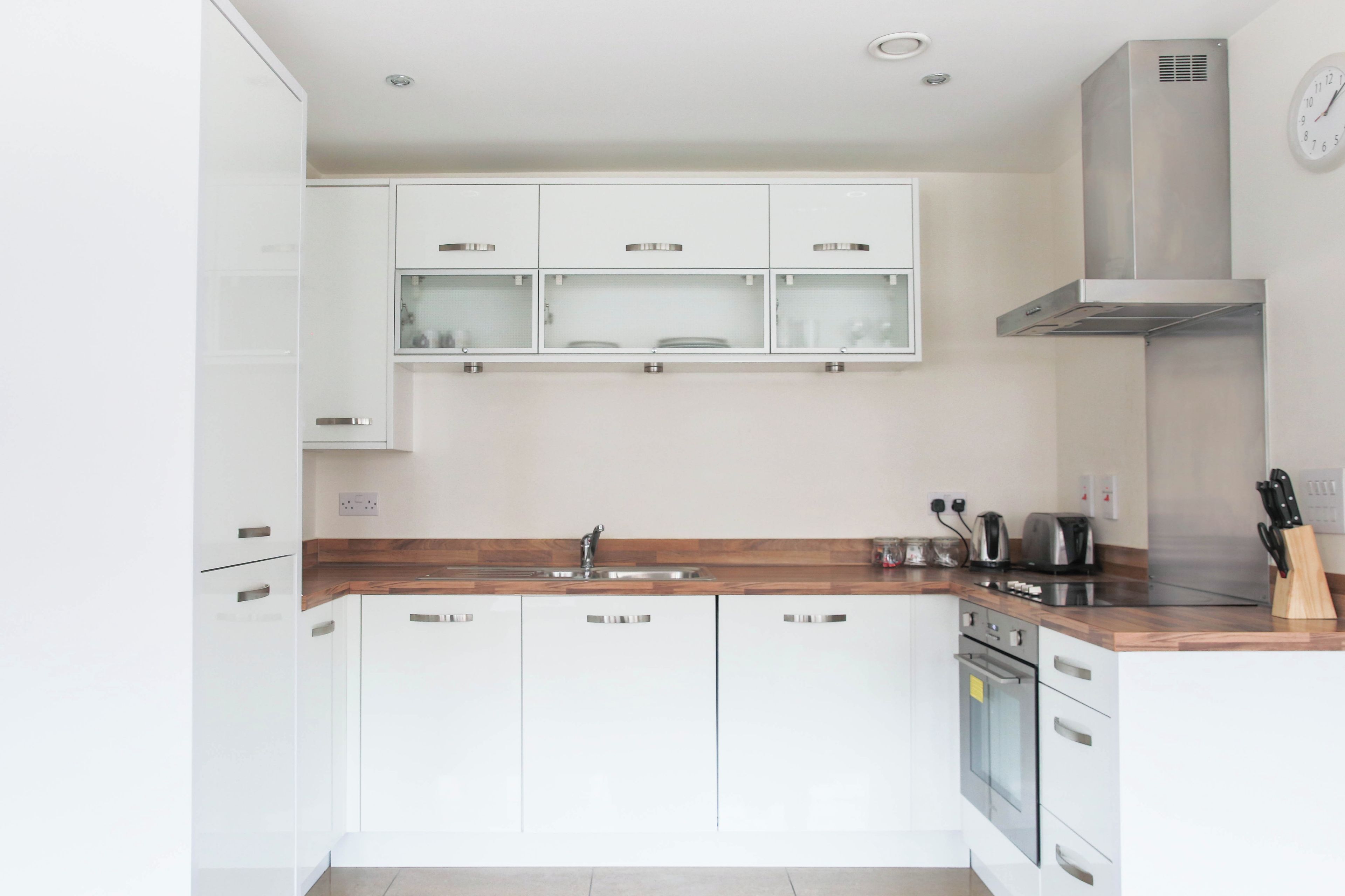A modern kitchen with white cabinets, a wooden countertop, a stainless steel sink, and a built-in oven.