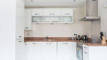 A modern kitchen with white cabinets, a wooden countertop, a stainless steel sink, and a built-in oven.
