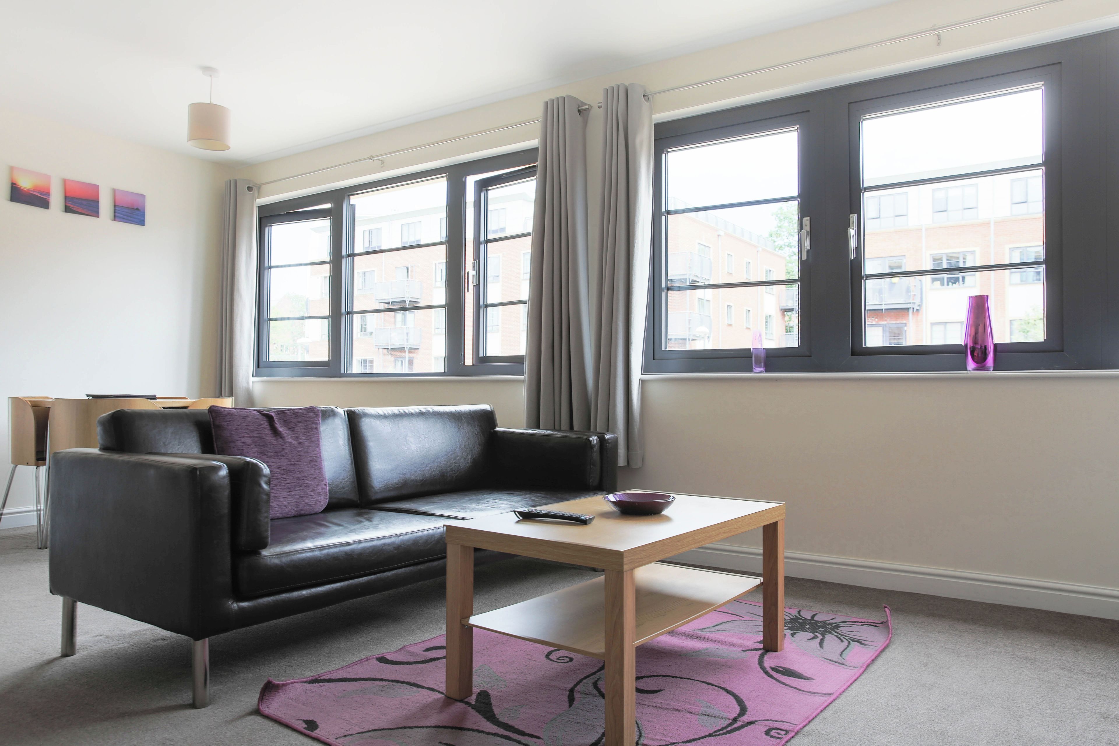 A modern living room with a black leather sofa, a wooden coffee table, and a view of the city through large windows.