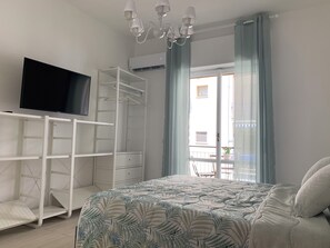 Un dormitorio con cama, televisor en un mueble, armario y balcón con una silla.
