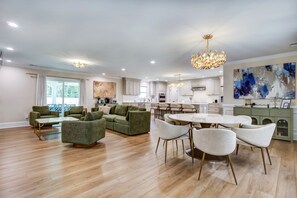 Een moderne woonkamer met een groene zithoek, een eethoek met een ronde tafel en een keuken met witte kasten.