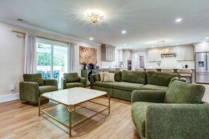 Een moderne woonkamer met een groene zithoek, een salontafel en een eethoek, met een keuken op de achtergrond.