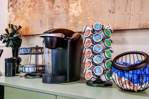 Eine Kaffeemaschine, eine Kapselhalterung und ein Tablett mit Kaffeetassen auf einer Arbeitsplatte.