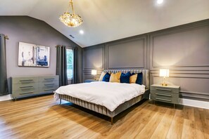Een slaapkamer met een groot bed, nachtkastjes, een kroonluchter en een schilderij aan de muur.