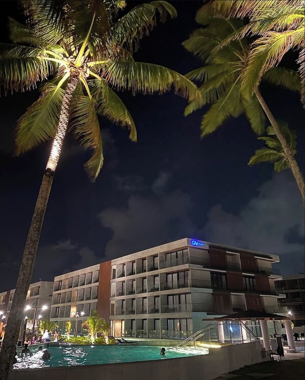 Een hotel met een zwembad, palmbomen en een moderne gevel.