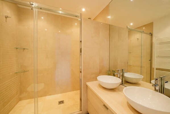 Un baño moderno con ducha de vidrio, dos lavamanos y un espejo grande.