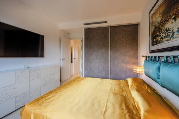 A bedroom with a bed, a TV, a painting, and a lamp. - New Listing (Cannes)