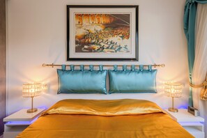 Un dormitorio con una cama, dos mesitas de noche con lámparas, un cuadro enmarcado sobre la cama y una cortina en la ventana.