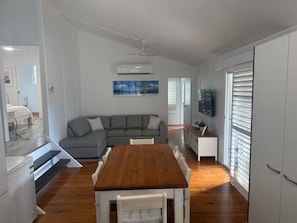 Ein moderner Wohnraum mit Esstisch aus Holz, grauem Sofa und einem an der Wand befestigten Flachbildfernseher.