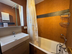 Ein Badezimmer mit einem weißen Waschbecken, einem Spiegel, einer Dusche inklusive Duschbrause und einem Handtuchhalter.