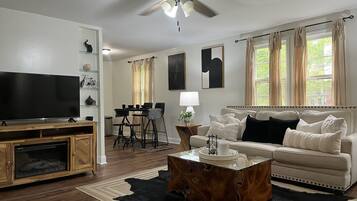 Ein Wohnzimmer mit Fernseher, Deckenventilator, einer Couch, einem Couchtisch und einem Essbereich mit Stühlen und einem Tisch.