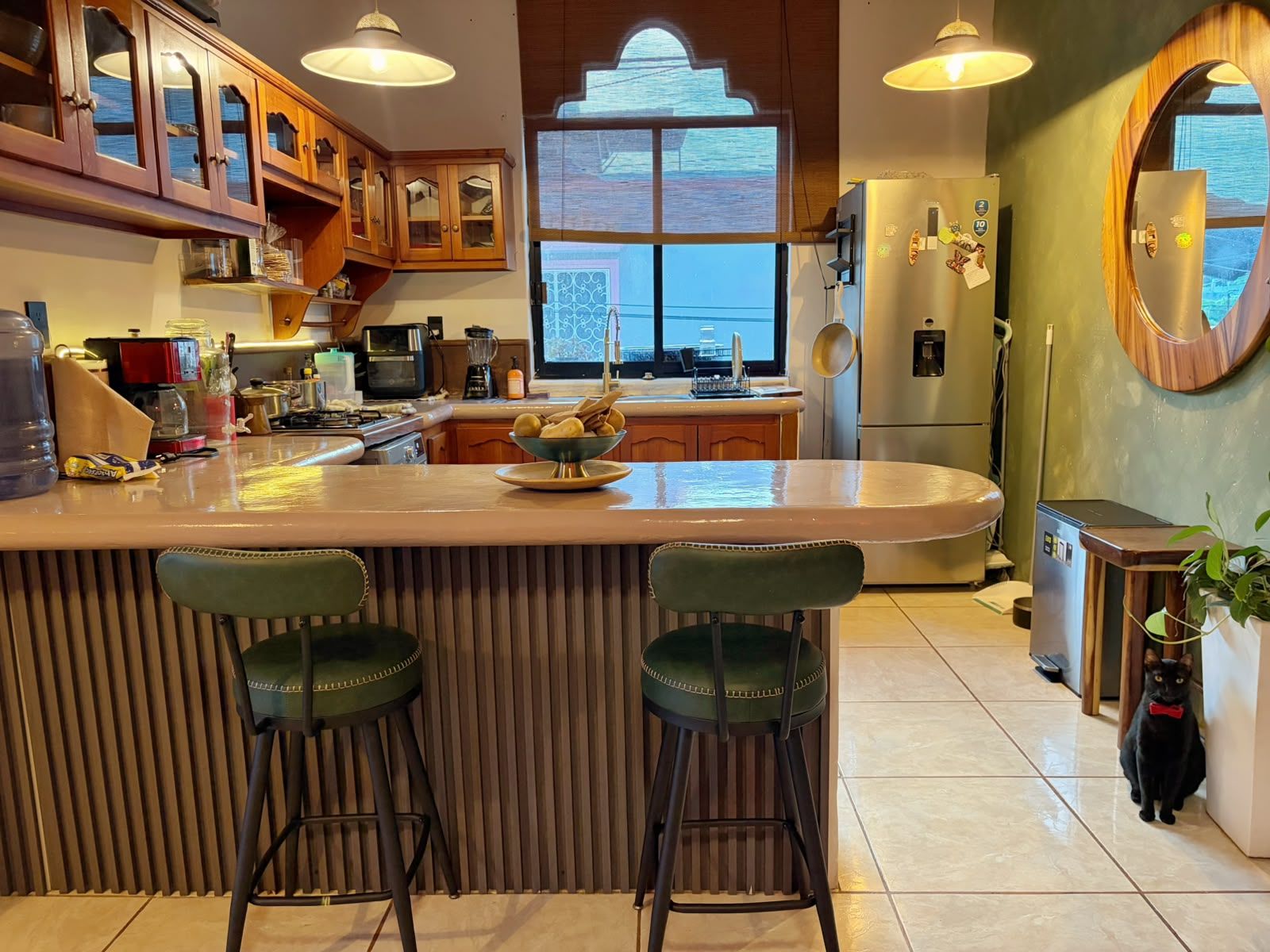 A kitchen with a central island, bar stools, a refrigerator, and a window with a view.