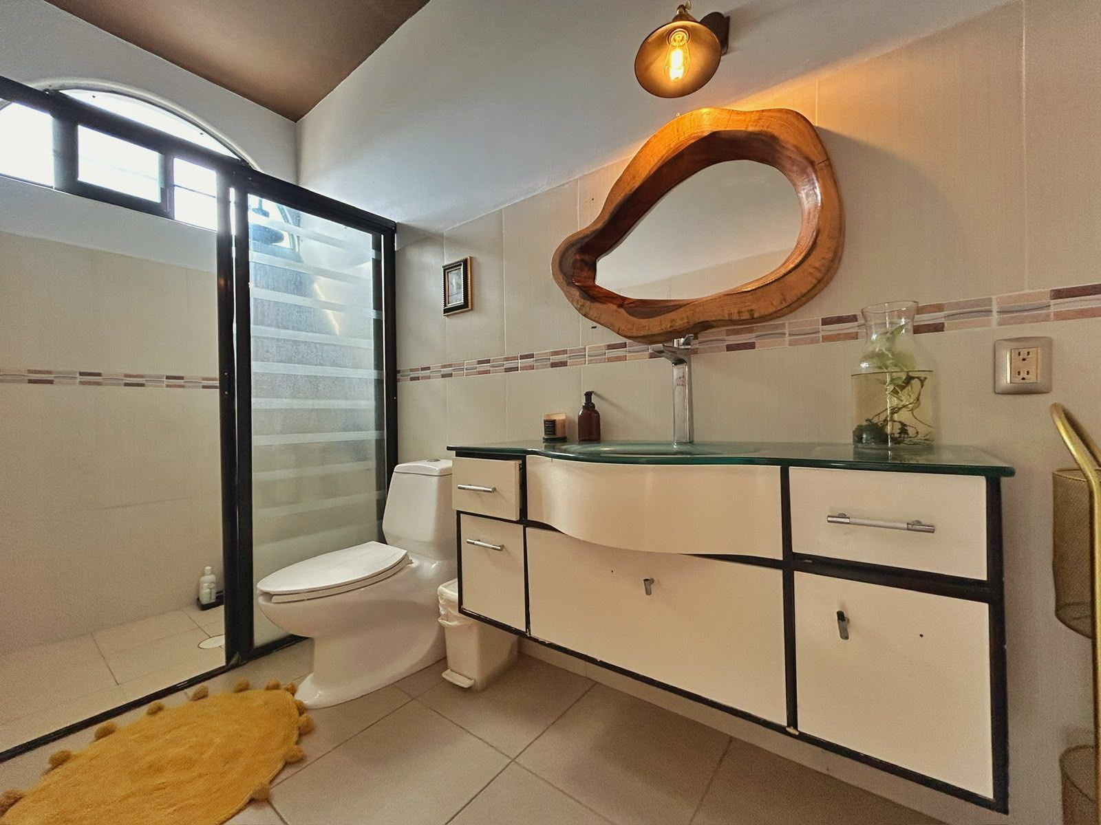 A bathroom with a toilet, a vanity with drawers, a mirror, and a light fixture.