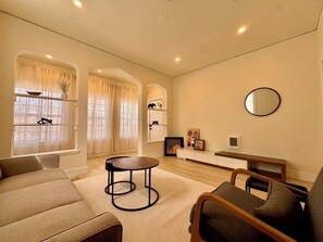 A modern living room with a sofa, a round coffee table, and a TV. There is a window with curtains and a mirror on the wall. - New Renovated 1B1B Coastal Living Near UCSF & Golden Gate Park (San Francisco)