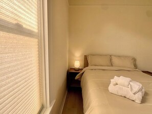 A hotel room with a bed, a nightstand with a lamp, and a window with blinds. - New Renovated 1B1B Coastal Living Near UCSF & Golden Gate Park (San Francisco)