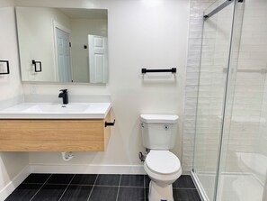 A bathroom with a white sink, a toilet, a mirror, and a glass shower enclosure. - New Renovated 1B1B Coastal Living Near UCSF & Golden Gate Park (San Francisco)