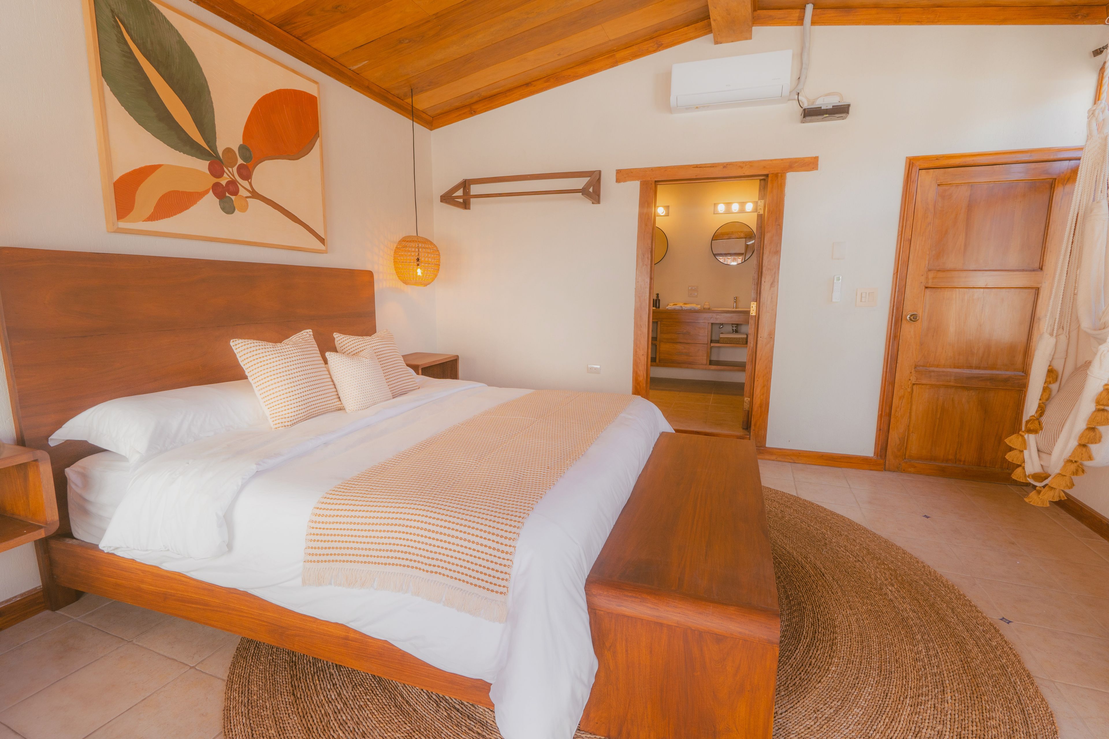 Quarto com cama de madeira, mesa de cabeceira, luminária na parede e porta para um banheiro.