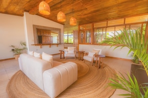 A modern living room with a sofa, chairs, a coffee table, and a large window. - Flor de café (Juayúa)