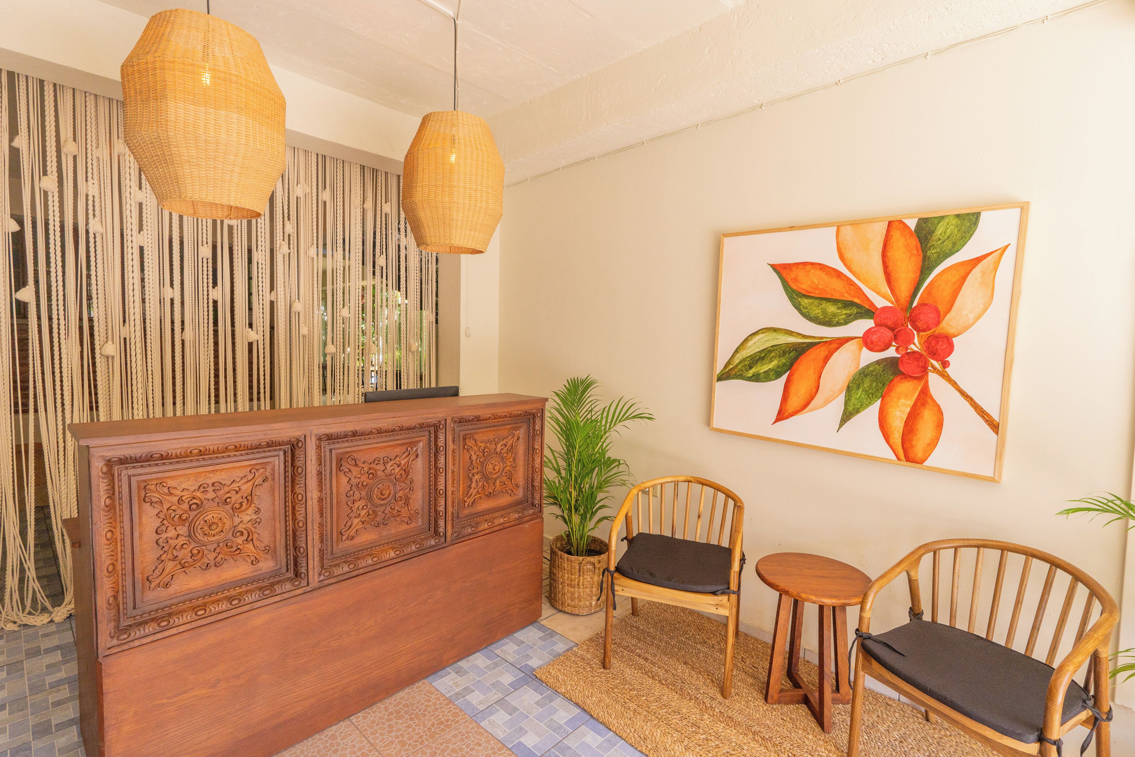 A reception area with a wooden reception desk, two wicker chairs, a potted plant, and a wall-mounted painting.